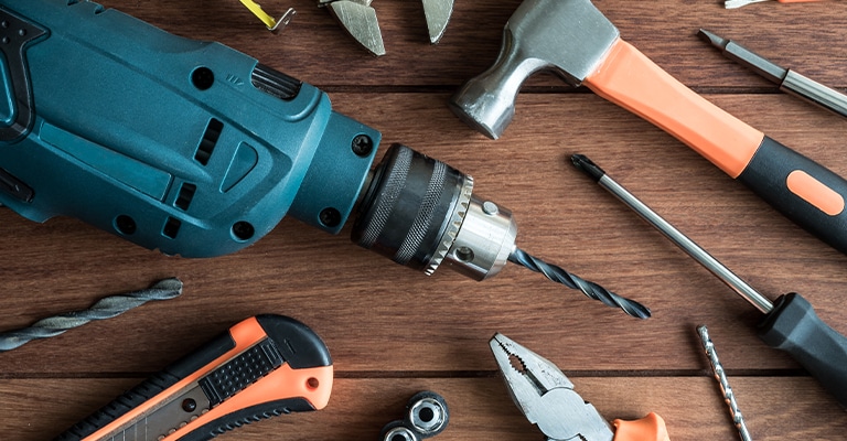OffPageSEO_11 • Andrew Roche SEO A variety of hand and power tools are arranged on a wooden surface, including a power drill with a bit attached, a hammer, pliers, a utility knife, screwdrivers, and drill bits. The image suggests DIY projects, construction, or home improvement work.