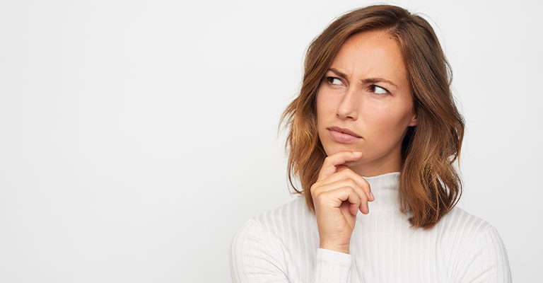 OffPageSEO_4 • Andrew Roche SEO A woman with shoulder-length brown hair wearing a white turtleneck top is looking up and to the side with a furrowed brow and her hand on her chin. Her expression suggests she is thinking deeply or feeling confused or uncertain.